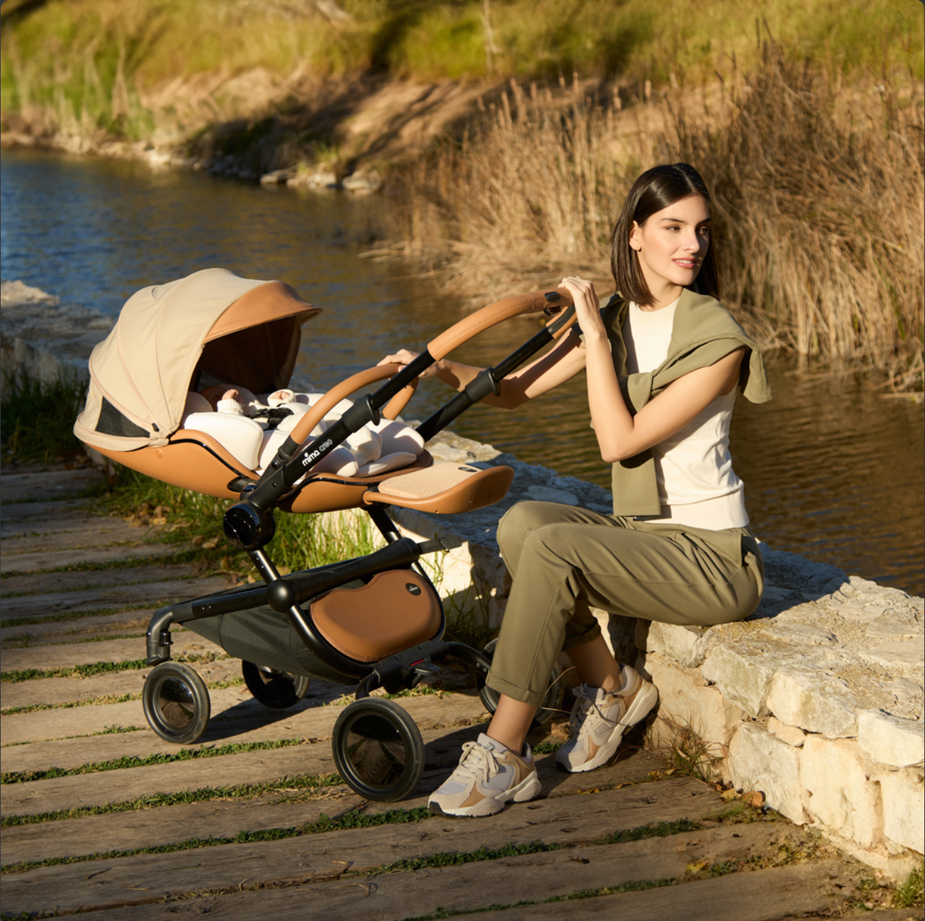 mother sitting by a creek next to mima creo stroller in mocha cream color with snuggle installed