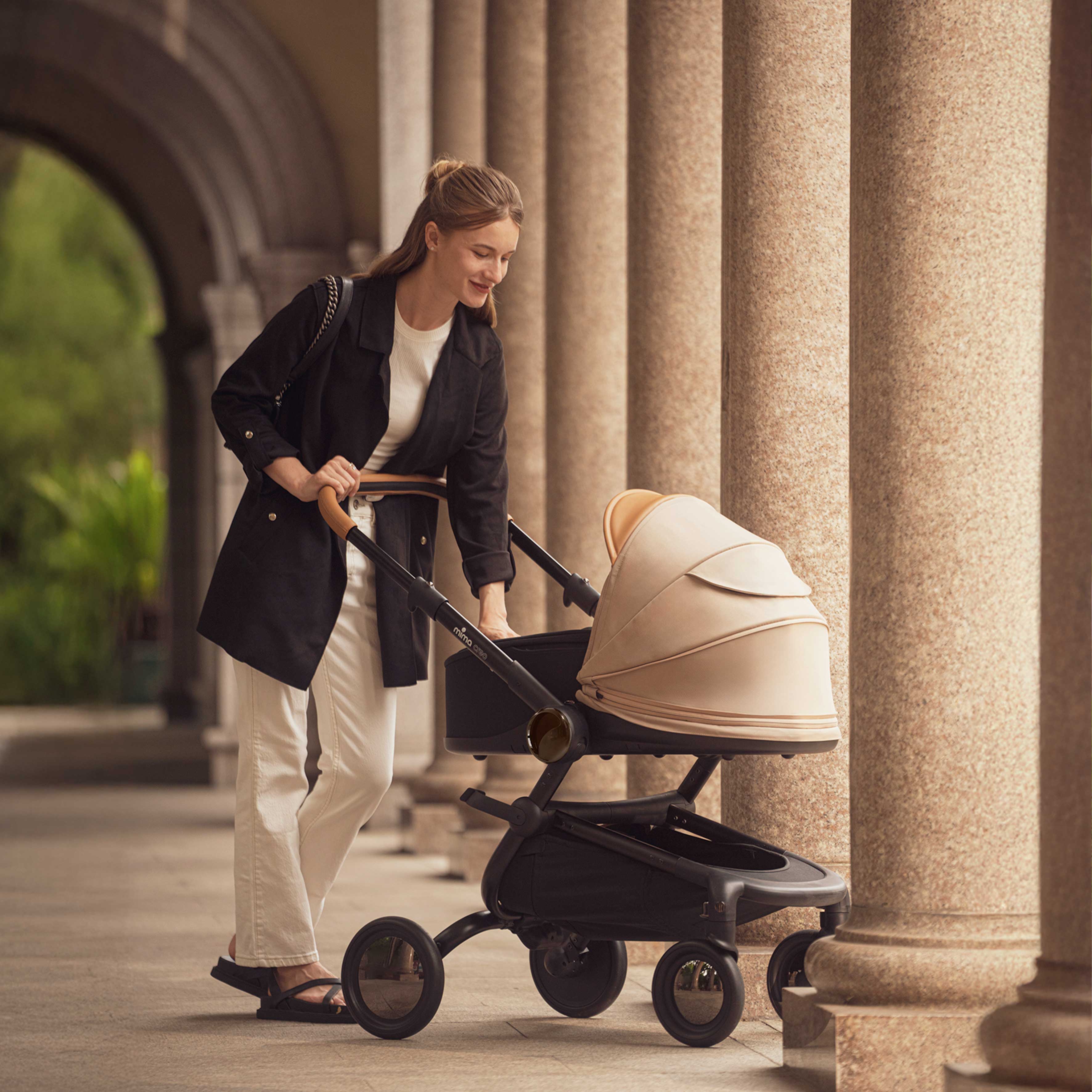 Mima® Creo Mocha Cream Bassinet in a grand corridor with elegant columns, showcasing its cozy design and newborn-friendly features, perfect for stylish and comfortable strolls.