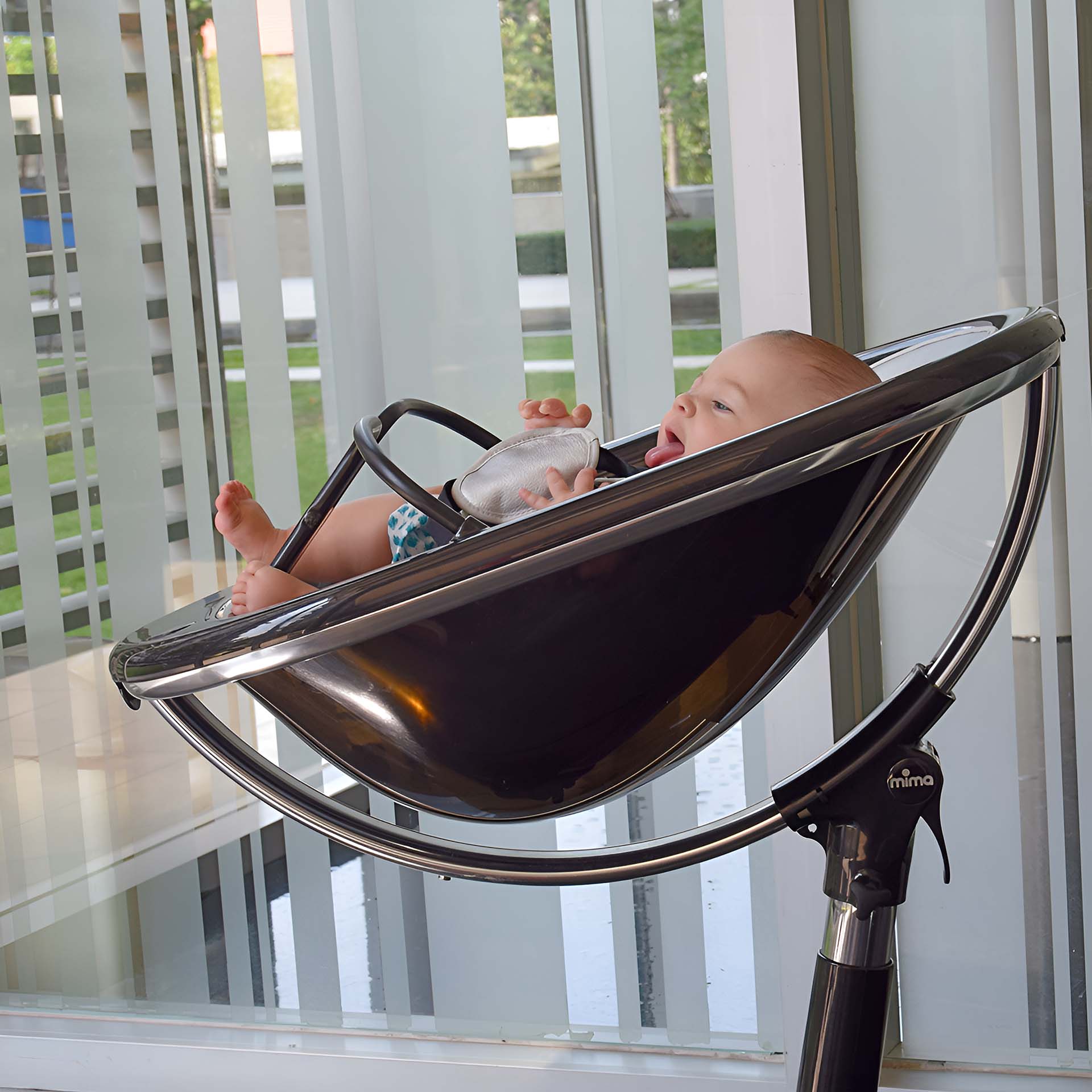 black Mima Moon 2G high chair in recline position with newborn, indoor near window