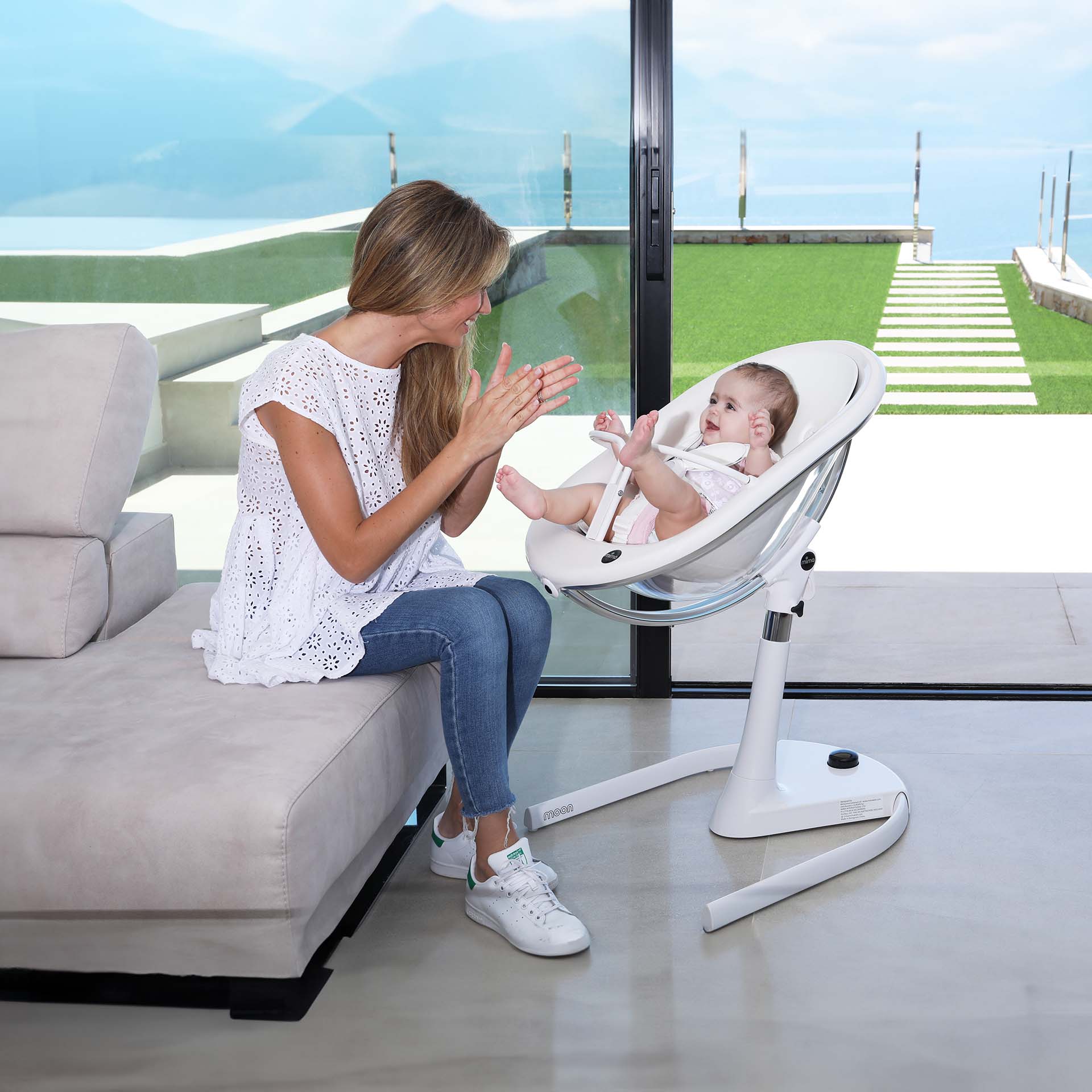 white Mima Moon 2G high chair in recline position with newborn, mother interacting, indoor with scenic view