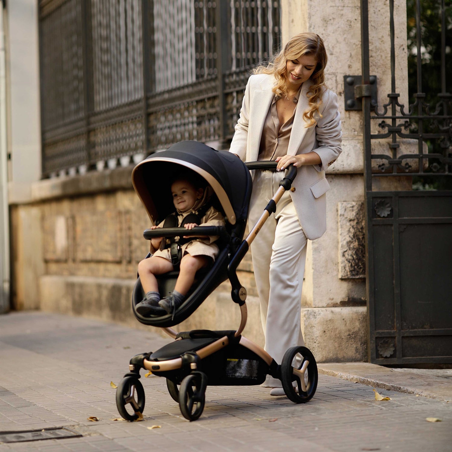 mima® xari max Black & Gold Special Edition with baby, mother in ivory coat pushing, side view on the street