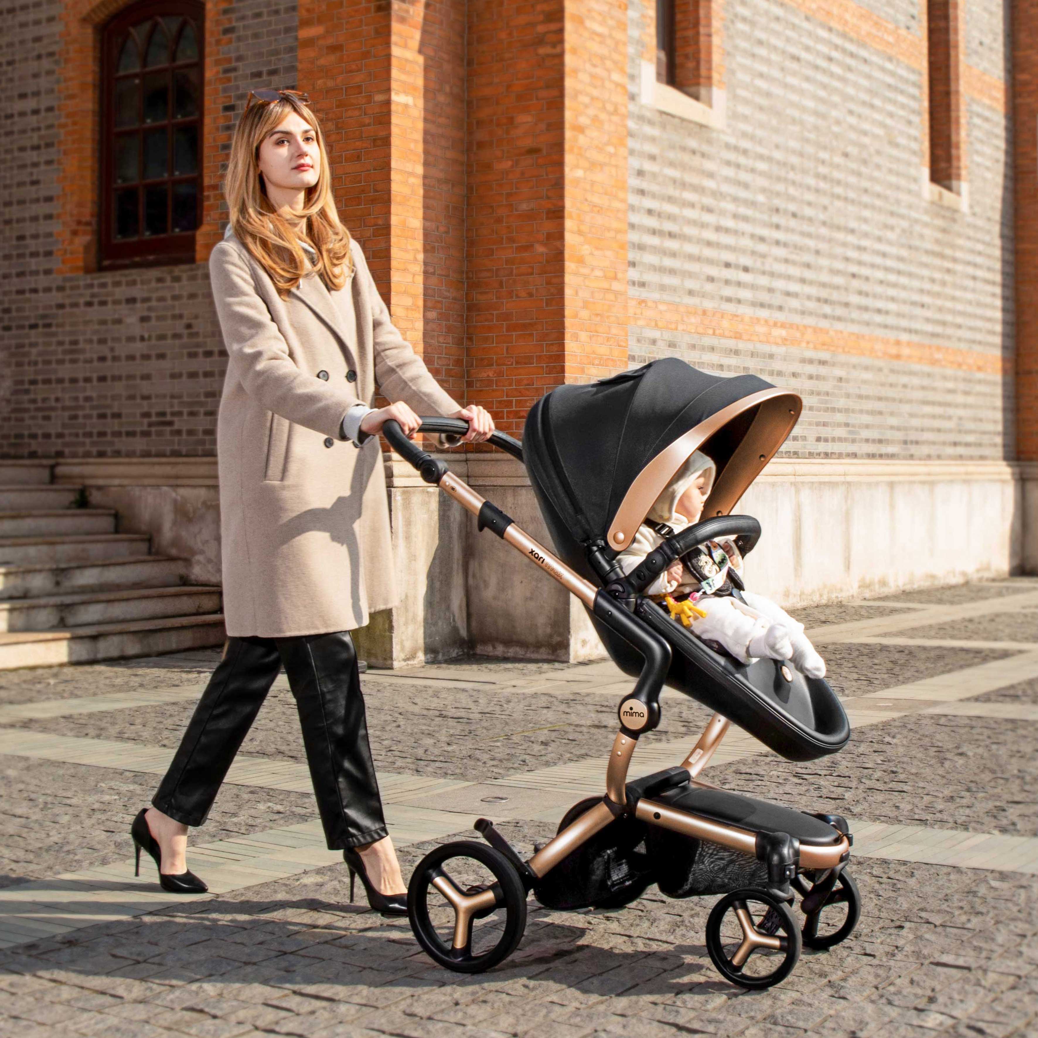 mima® xari max Black & Gold Special Edition with baby, mother in beige coat pushing, side view on street