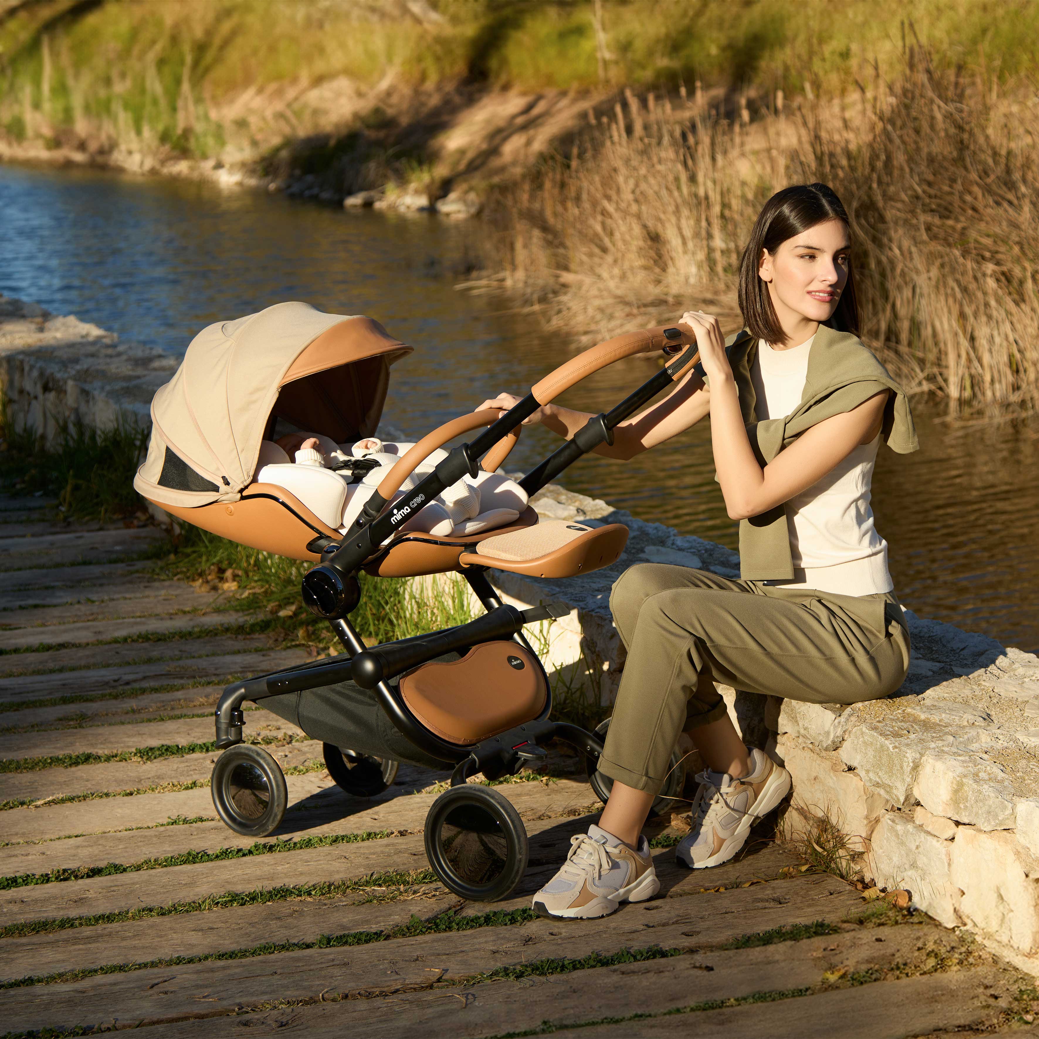 mother sitting by a creek next to mima creo stroller in mocha cream color with snuggle installed