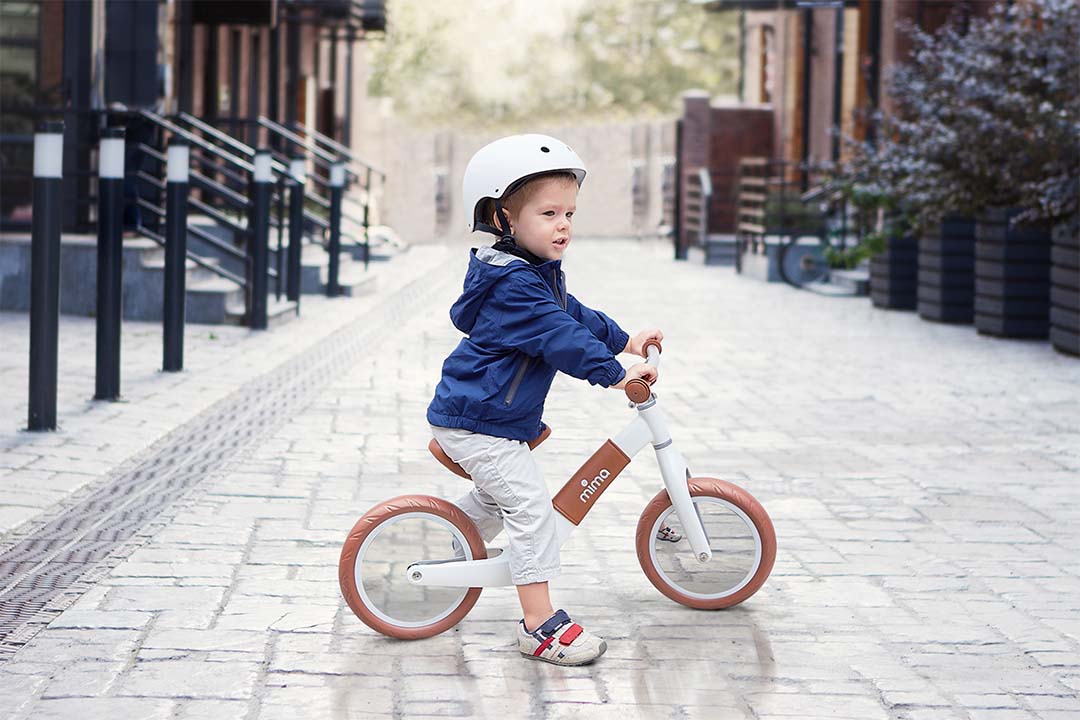 Boy wearing helmet, riding Mima® Zoom White balance bike