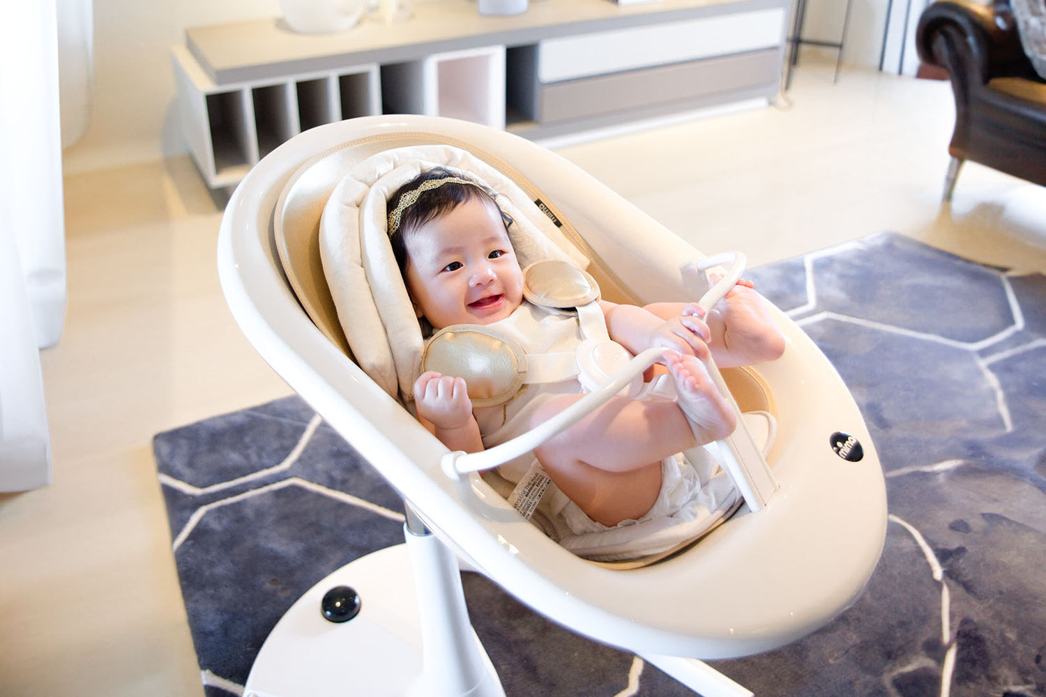 mima moon high chair with baby headrest, with a baby in lounger mode smiling, indoor living room