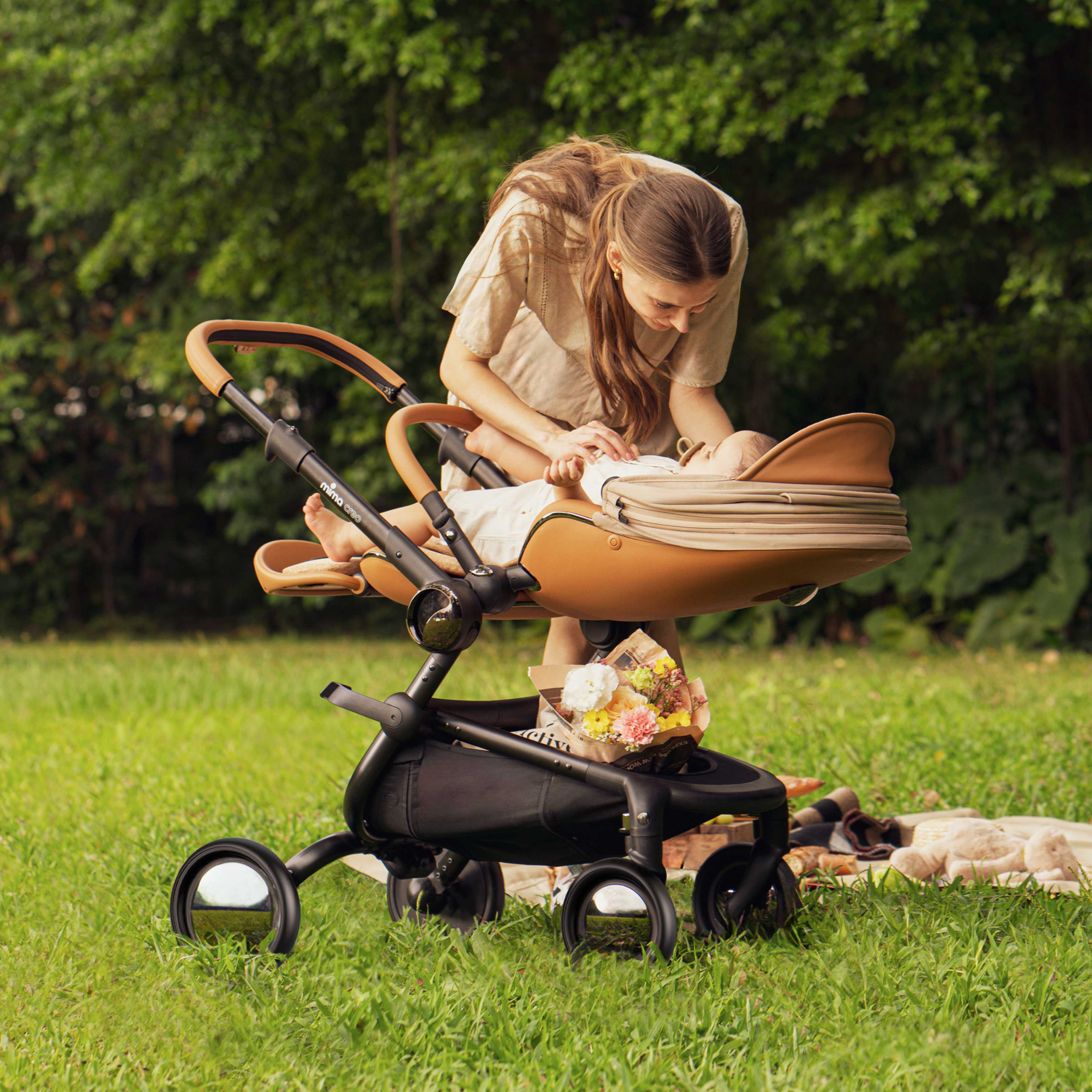 mother tending to baby in fully reclined parent facing mima creo stroller in mocha cream in a park