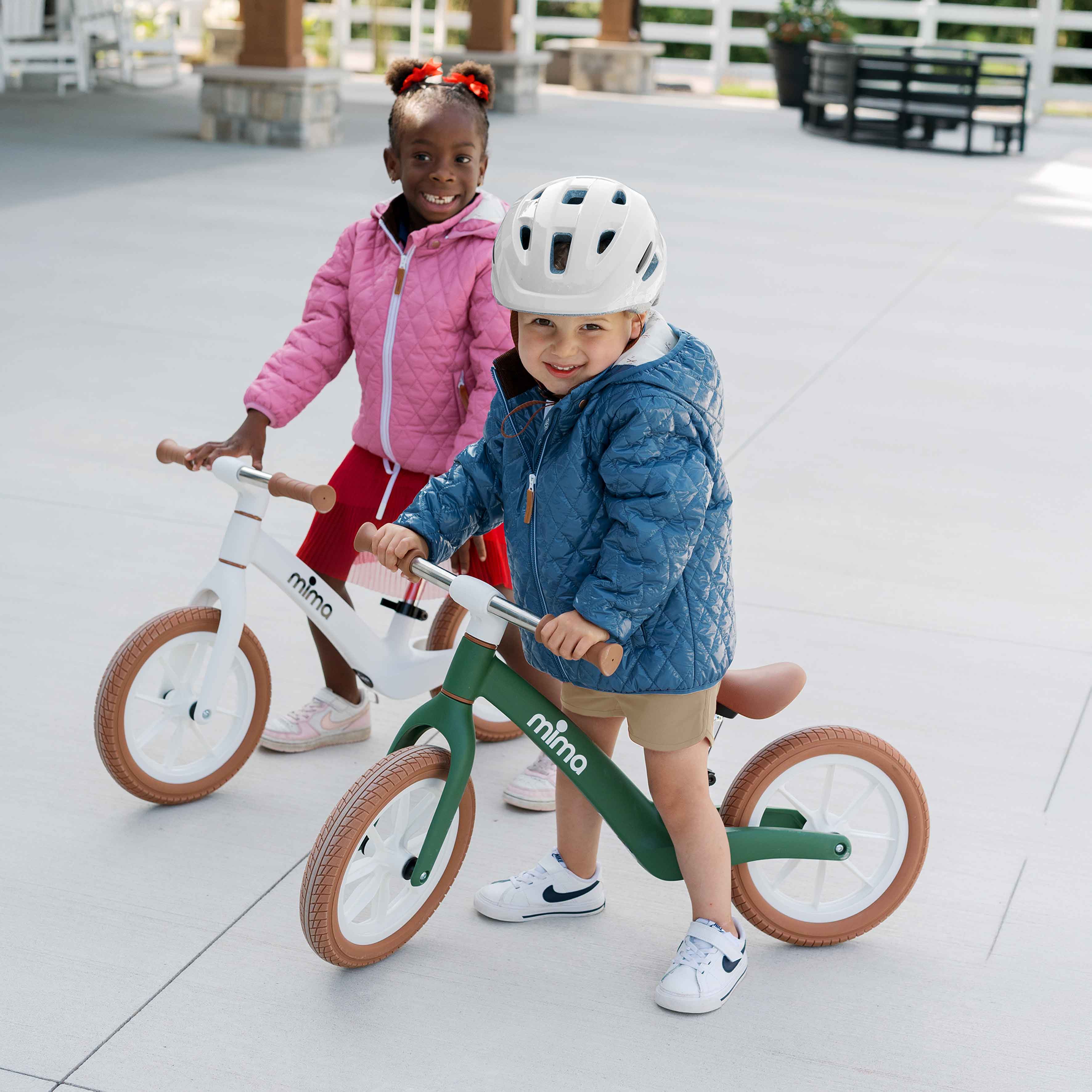 Two young children smiling and playing outdoors with green mima zoom lite balance bikes