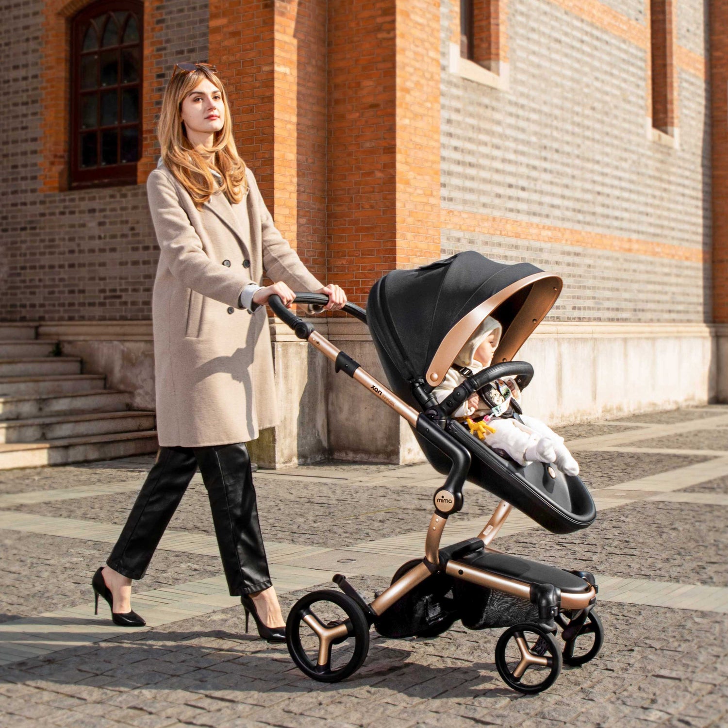 mima® xari max Black & Gold Special Edition with baby, mother in beige coat pushing, side view on street