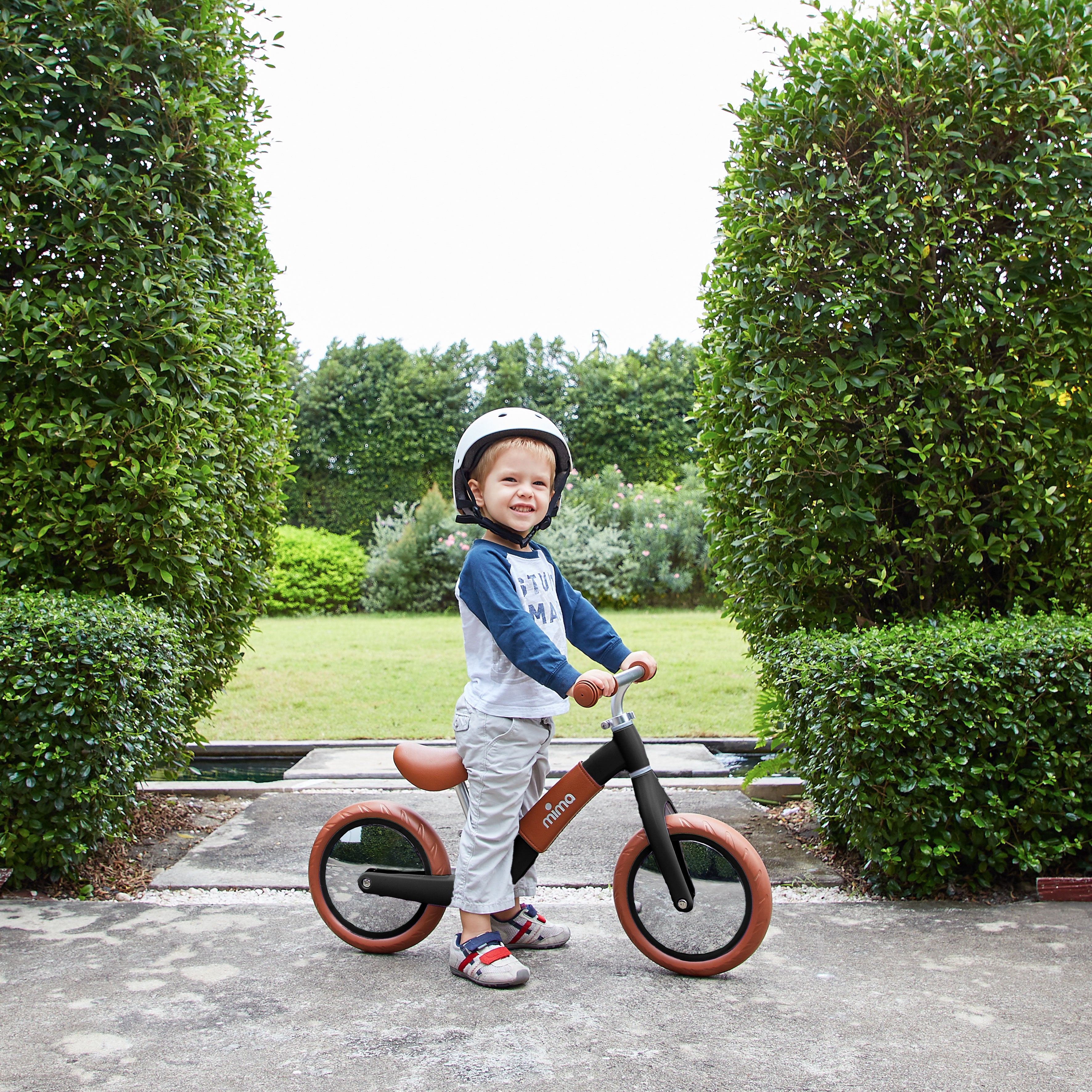 Mima Zoom Black balance bike in a park, surrounded by lush greenery and a grassy area, ideal for kids&