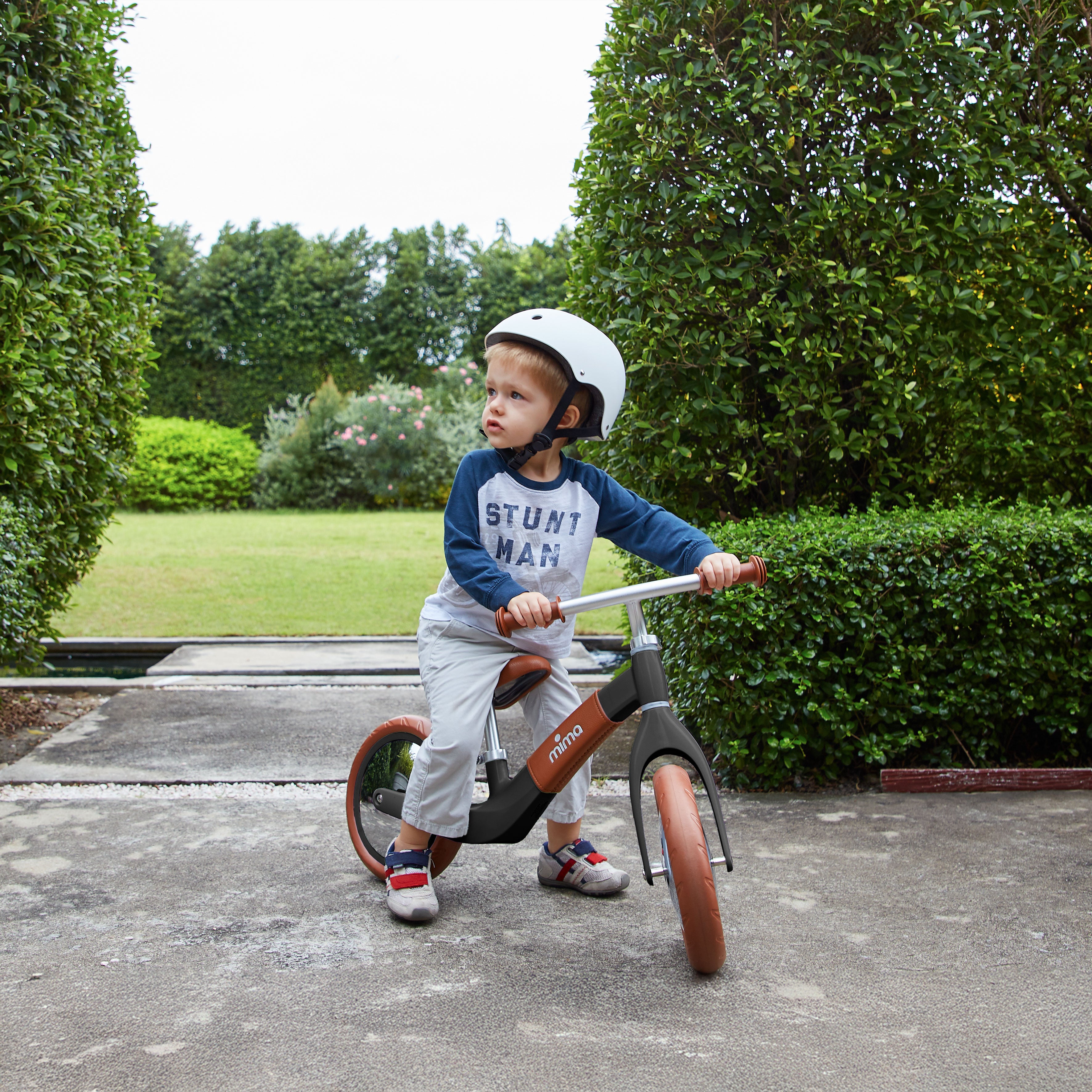 Mima Zoom Black balance bike in a park, surrounded by lush greenery and a grassy lawn, perfect for kids&