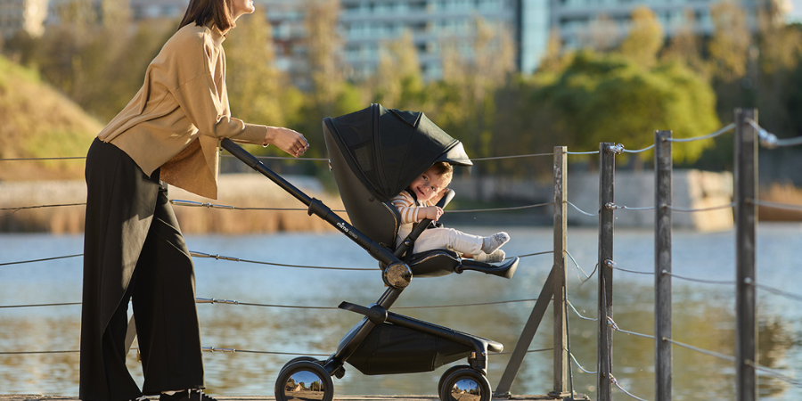 Newborn Stroller with Flat Recline mother with child in black stroller with chrome wheels at the lake in fall