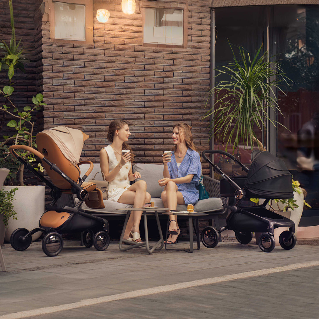 two mothers at outdoor cafe with mima creo mocha cream stroller and black bassinet for newborns