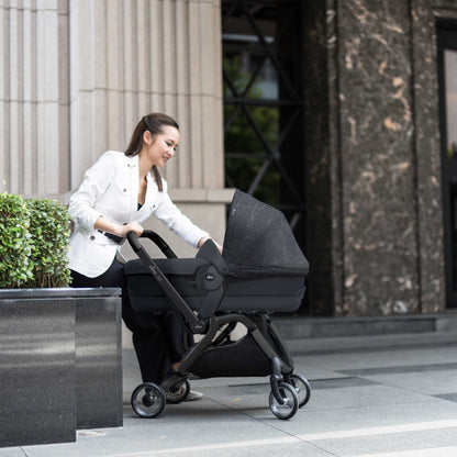 Mima® Zigi Bassinet in Ebony on a city street with a parent pushing, featuring a sleek black design and modern frame, ideal for urban baby transport.