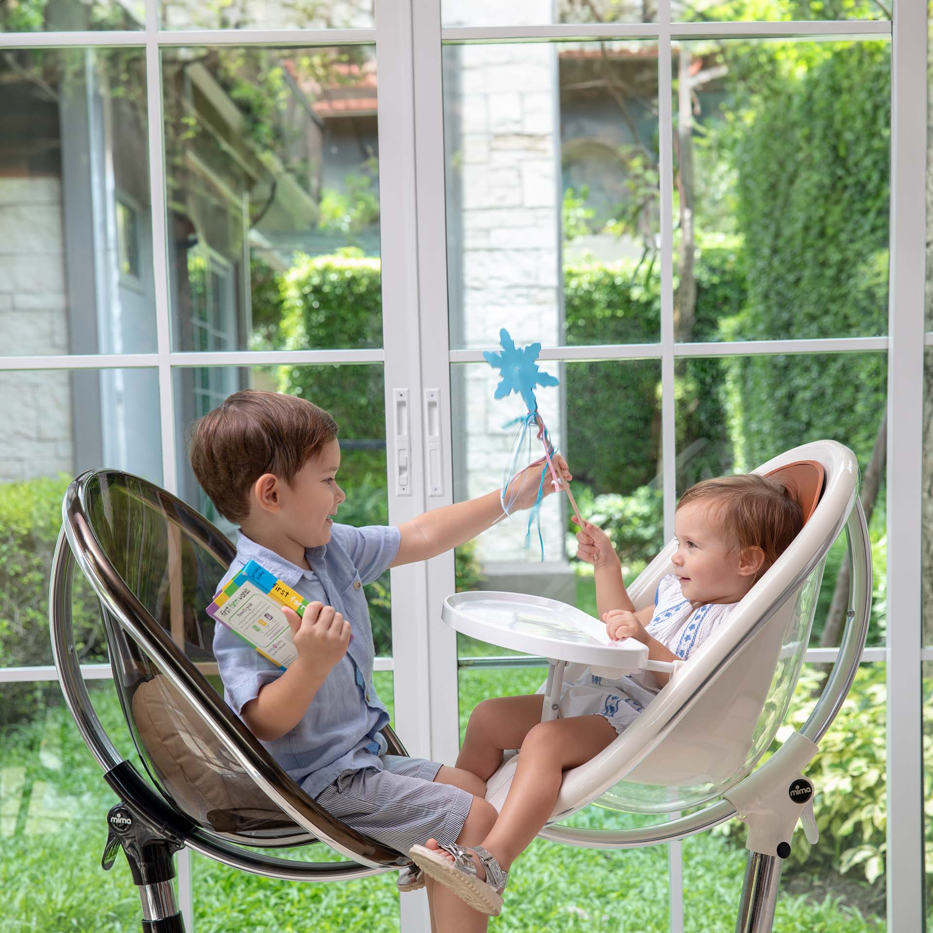 White Mima Moon 2G high chair in high chair mode and black Mima Moon 2G junior chair, children playing with toy, indoor near window  #color_white