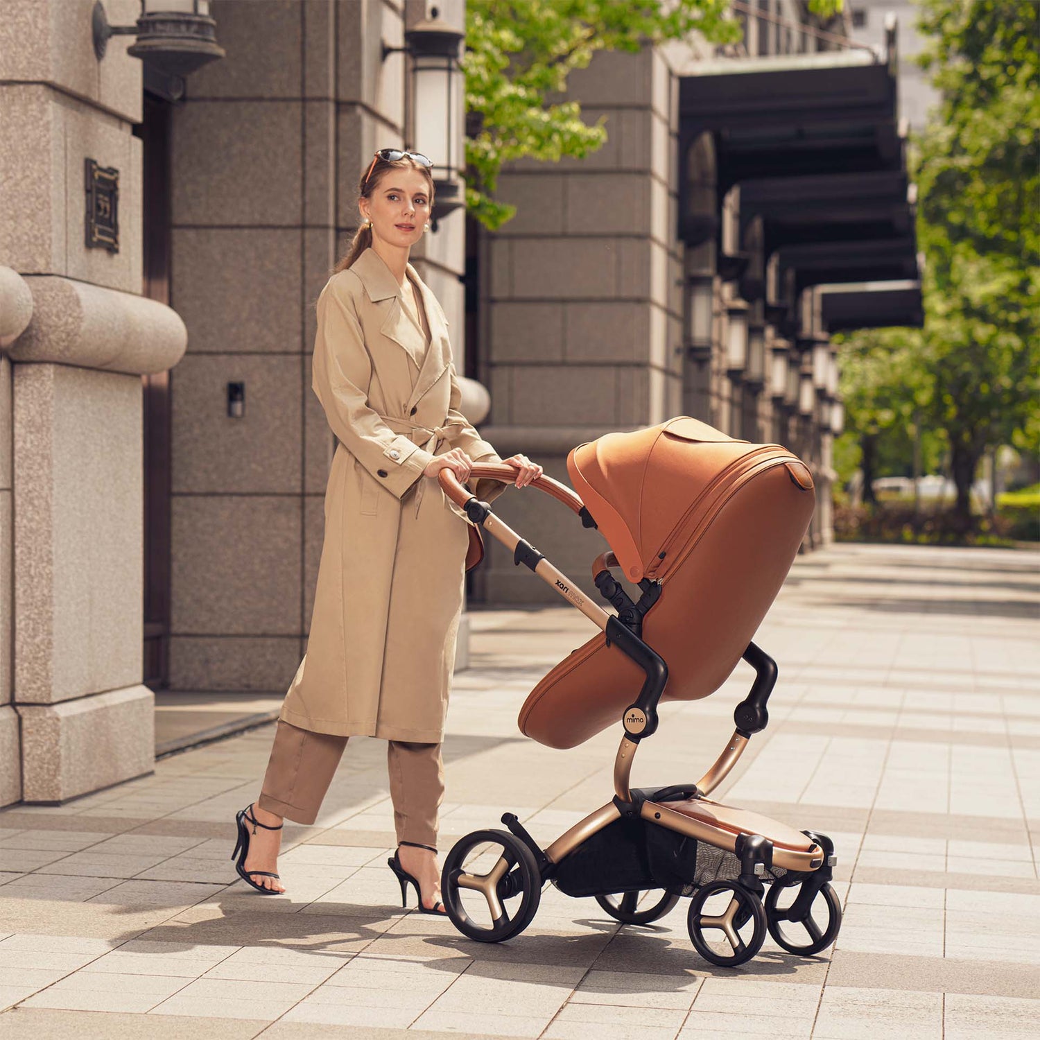 Camel mima Xari Max stroller with baby, mother in beige trench coat pushing, side view on street 