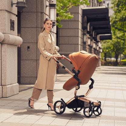 Camel mima Xari Max stroller with baby, mother in beige trench coat pushing, side view on street 
