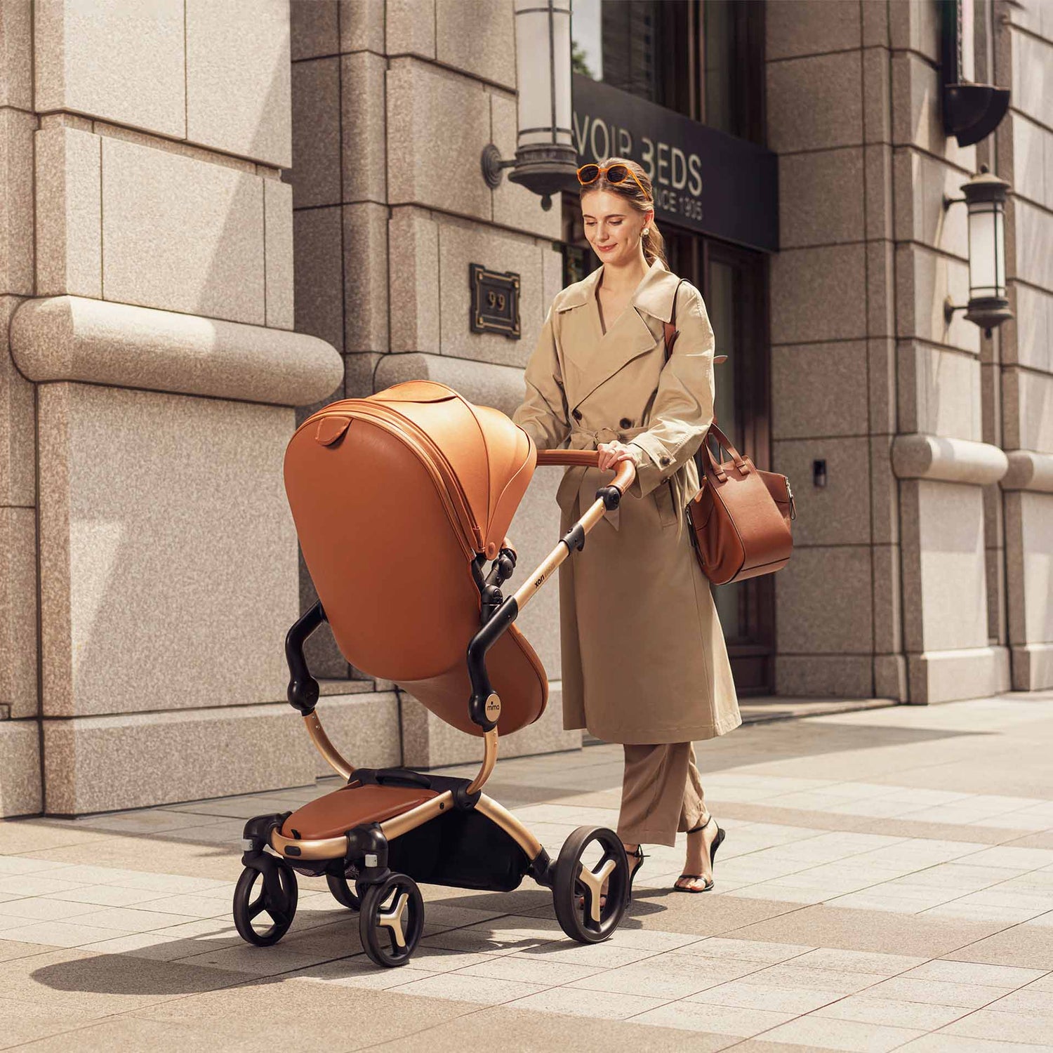 Camel mima Xari Max stroller with baby, mother in beige trench coat pushing, rear view on street 