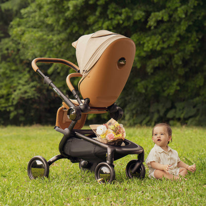 toddler boy sitting on the grass next to mima creo compact stroller in mocha cream viewed from behind 
