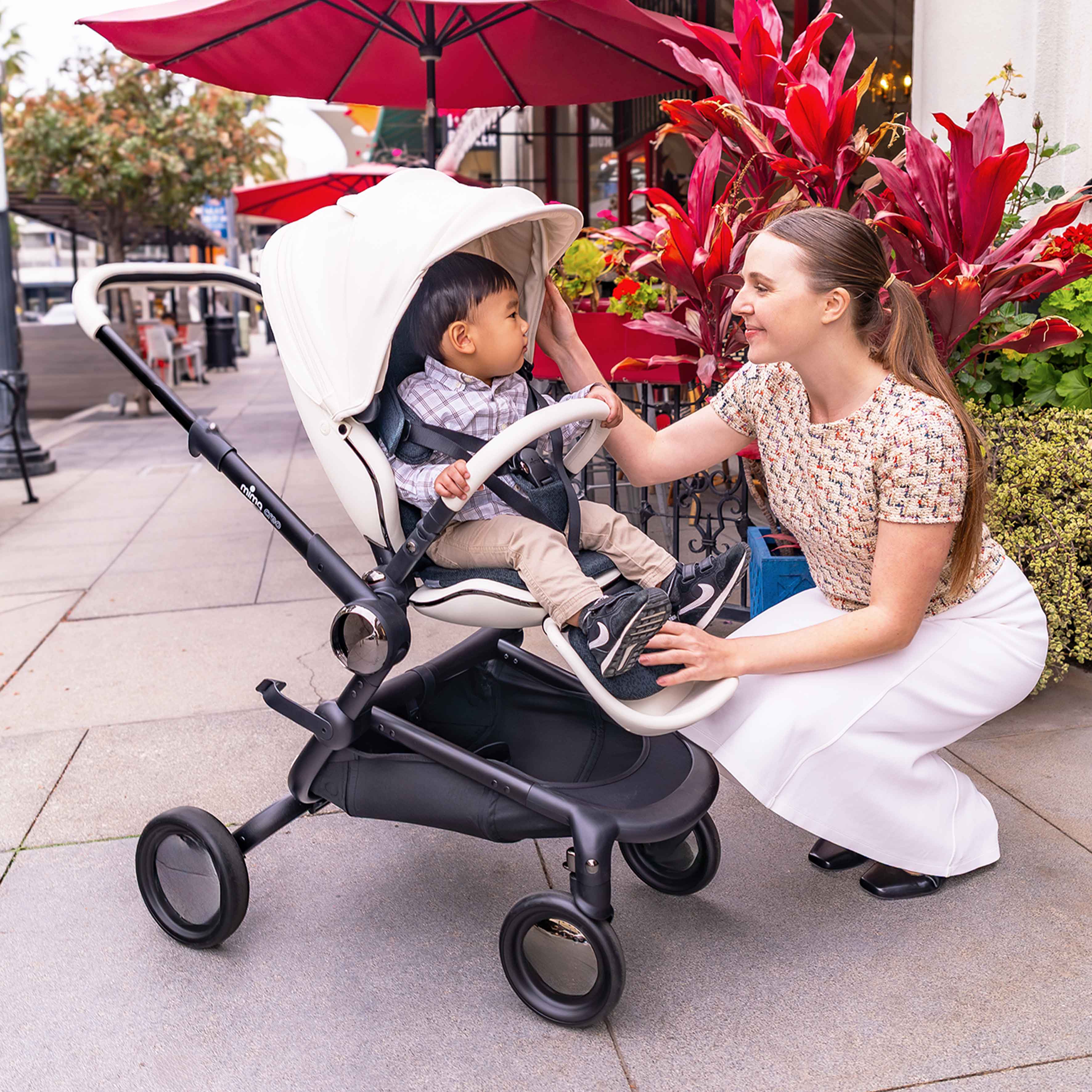 mother interacting with child in parent facing mima creo stroller in white under red umbrellas 