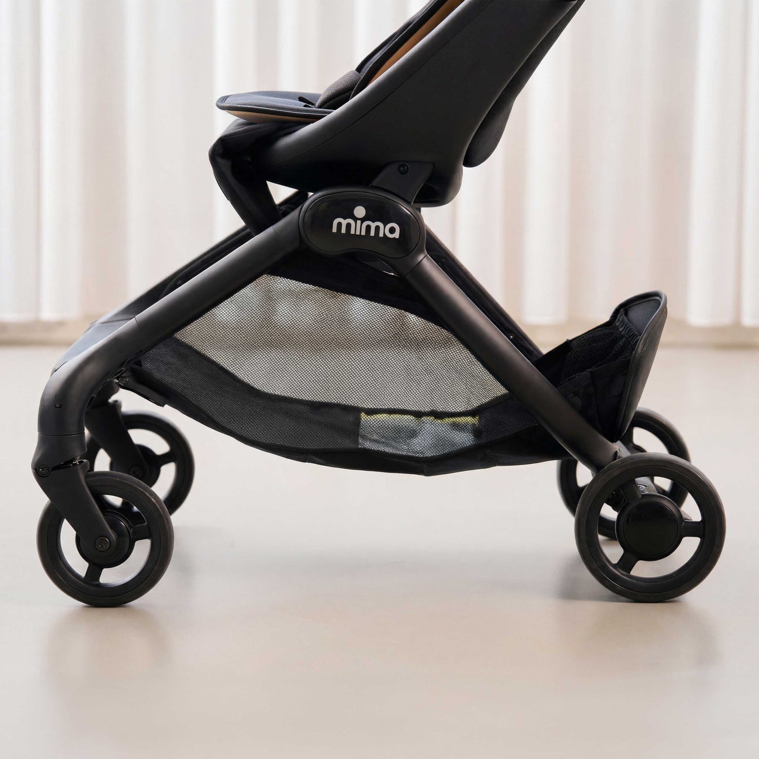 side detail view of chassis and storage basket on mima miro compact travel stroller in mocha 