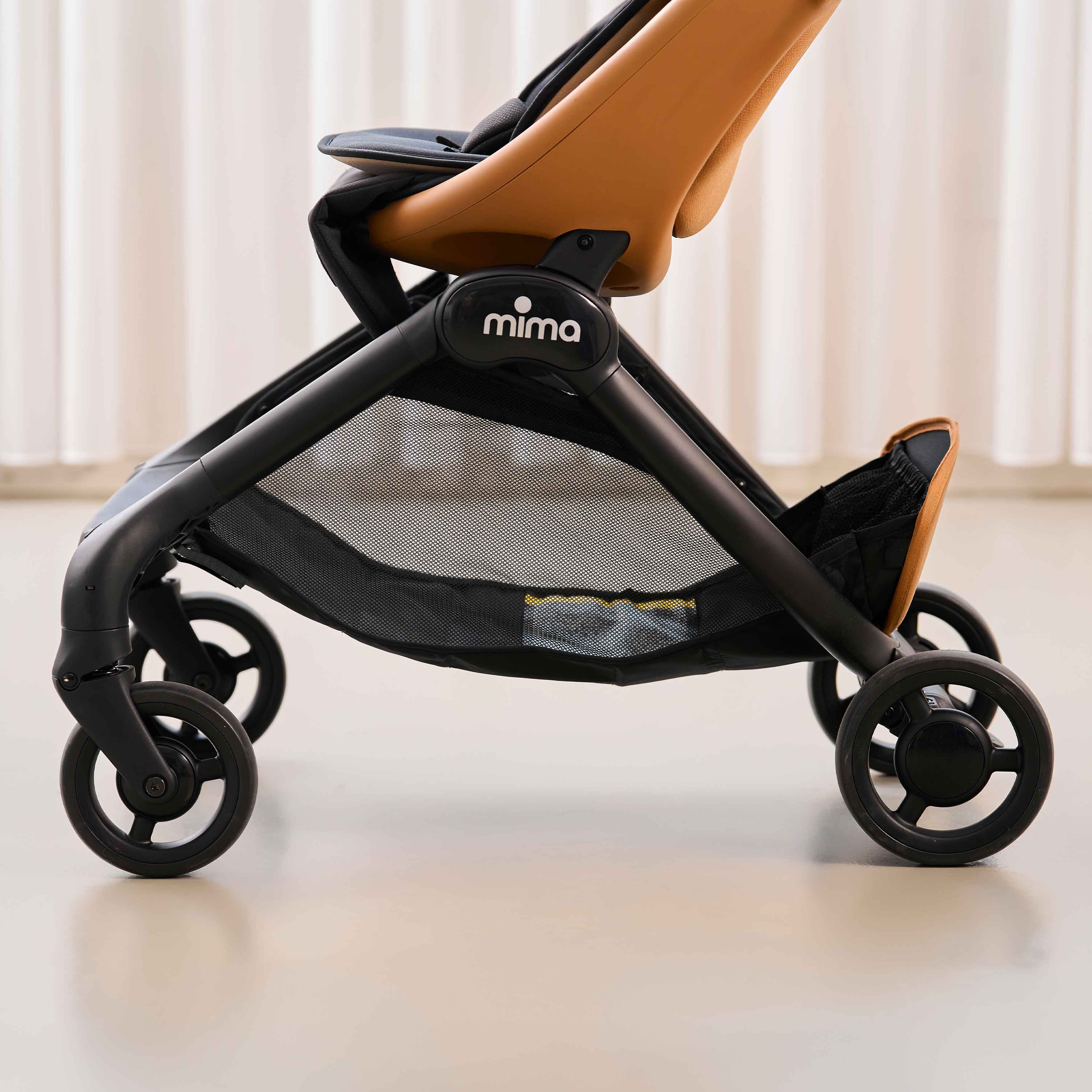 side detail view of chassis and storage basket on mima miro compact travel stroller in mocha cream 
