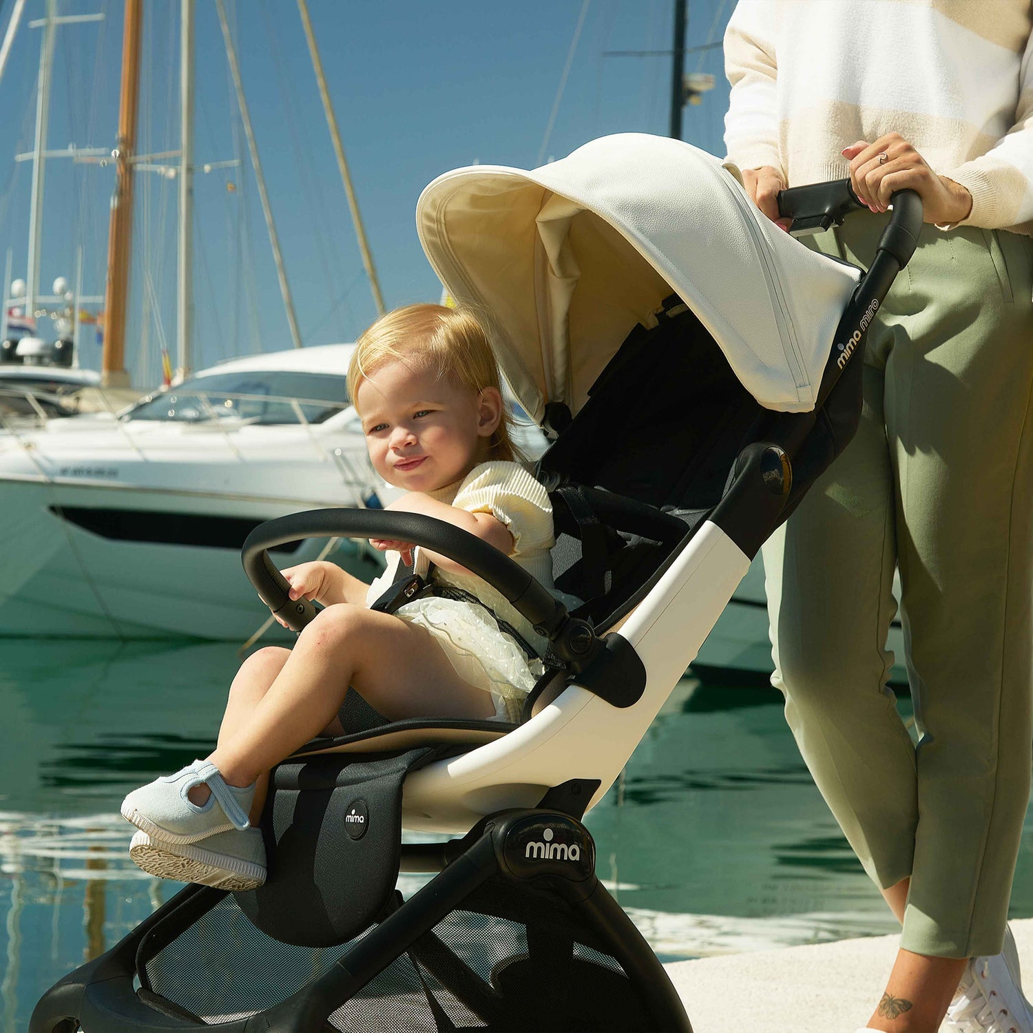 caregiver pushing miro compact travel stroller in white at a marina with yachts in the background 