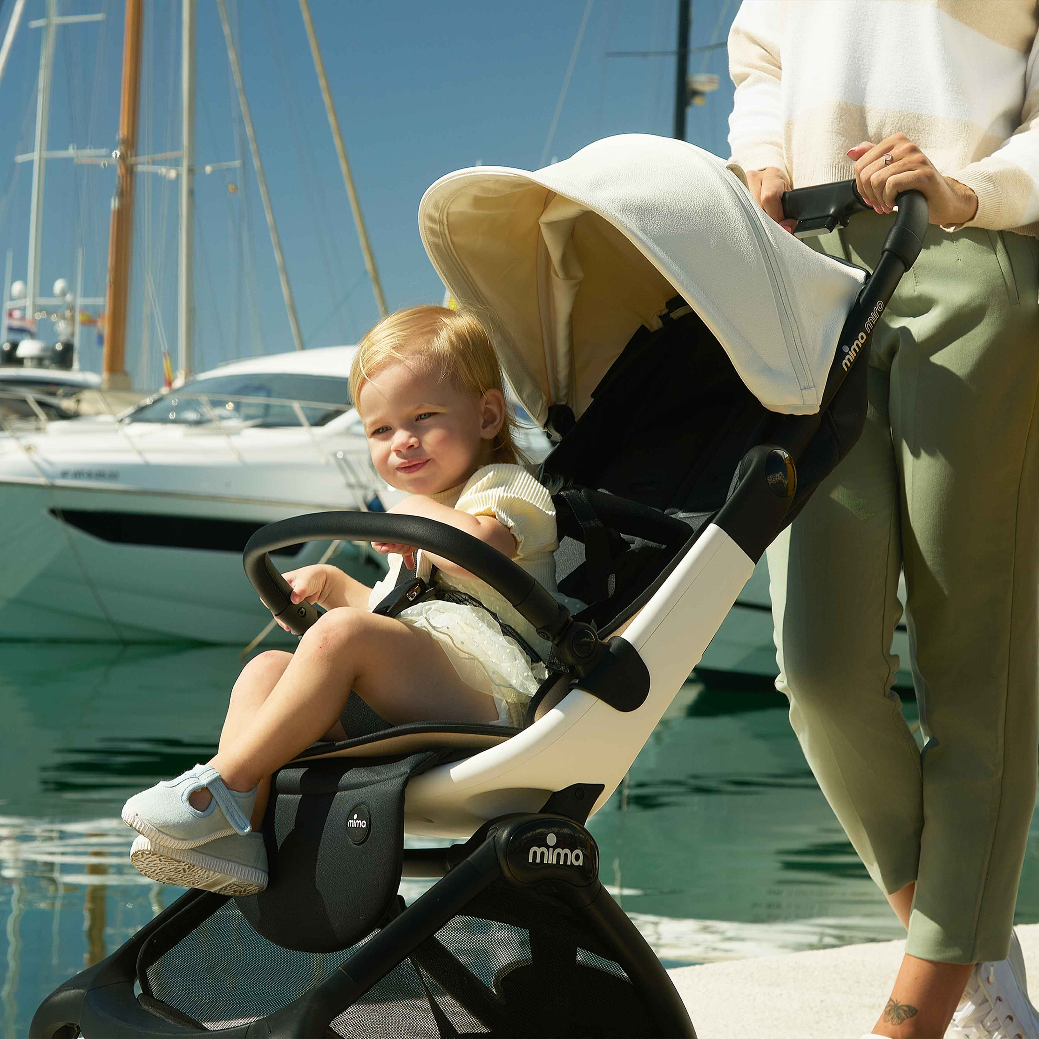 caregiver pushing miro compact travel stroller in white at a marina with yachts in the background 