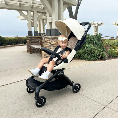 toddler girl sitting in mima miro compact travel stroller in white on a paved coastal path 