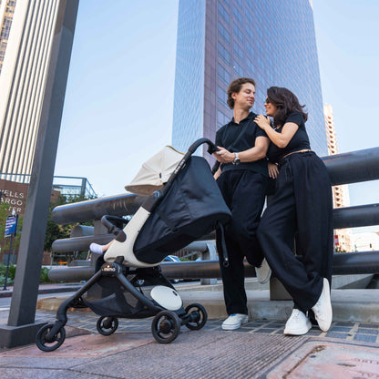 parents standing next to fully reclined mima miro stroller in white on a city street with skyscraper 