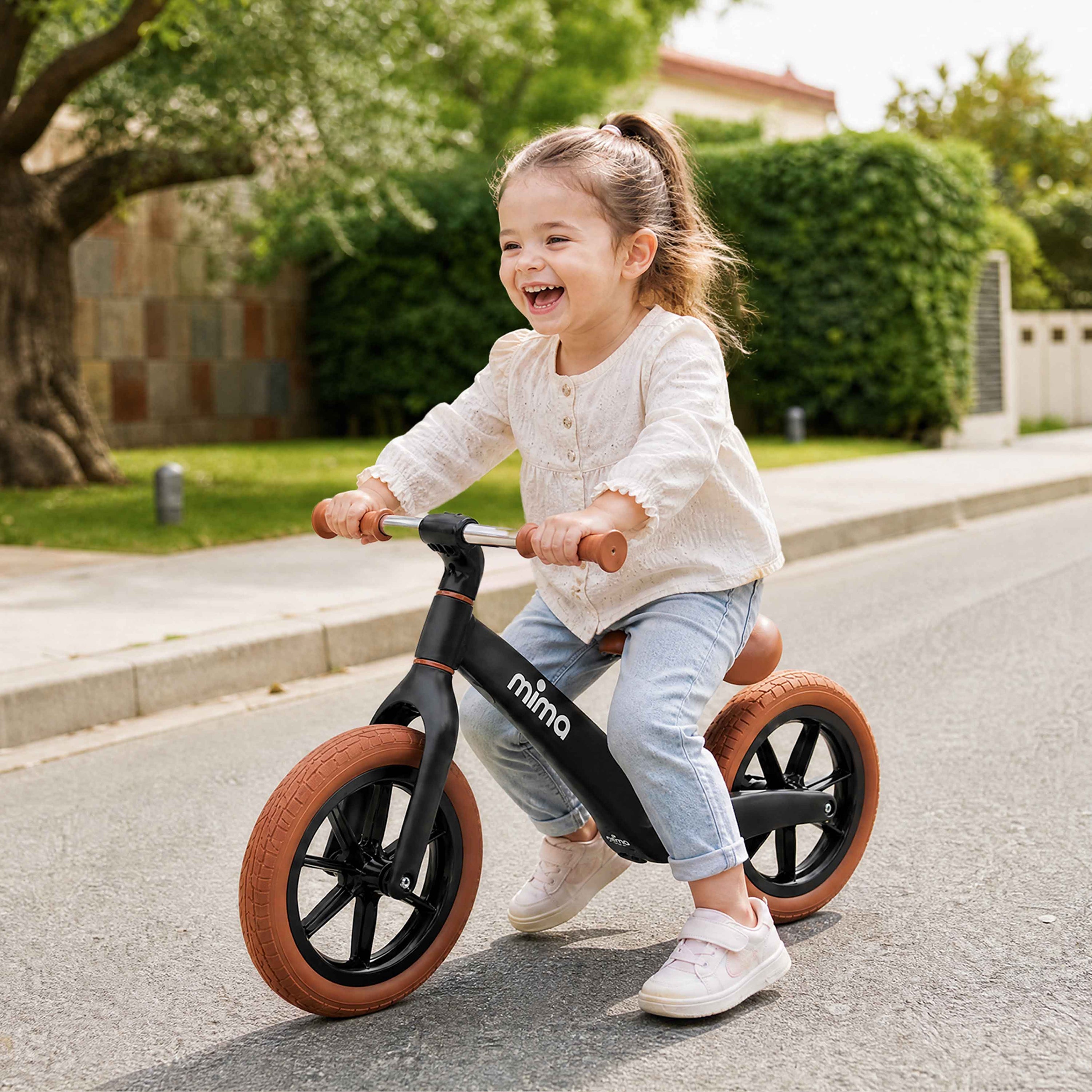 A laughing toddler having fun and riding a black mima zoom lite balance bike outdoors #color_black