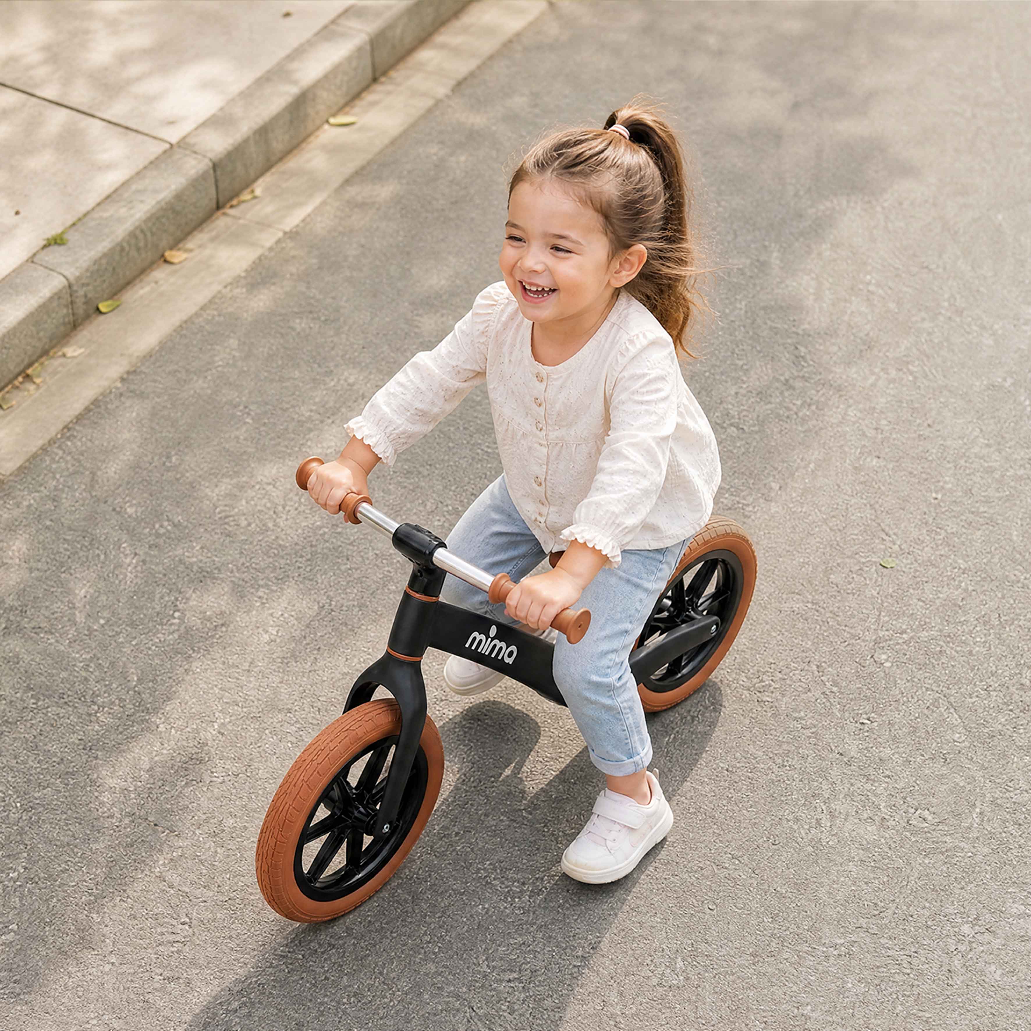 High-angle shot of a happy toddler riding a black mima zoom lite balance bike 