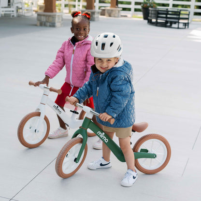 Two young children smiling and playing outdoors with green mima zoom lite balance bikes 