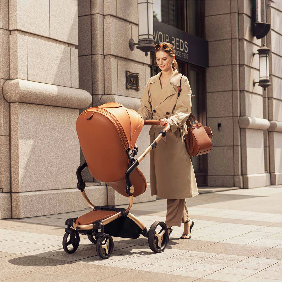 Camel mima Xari Max stroller with baby, mother in beige trench coat pushing, rear view on street